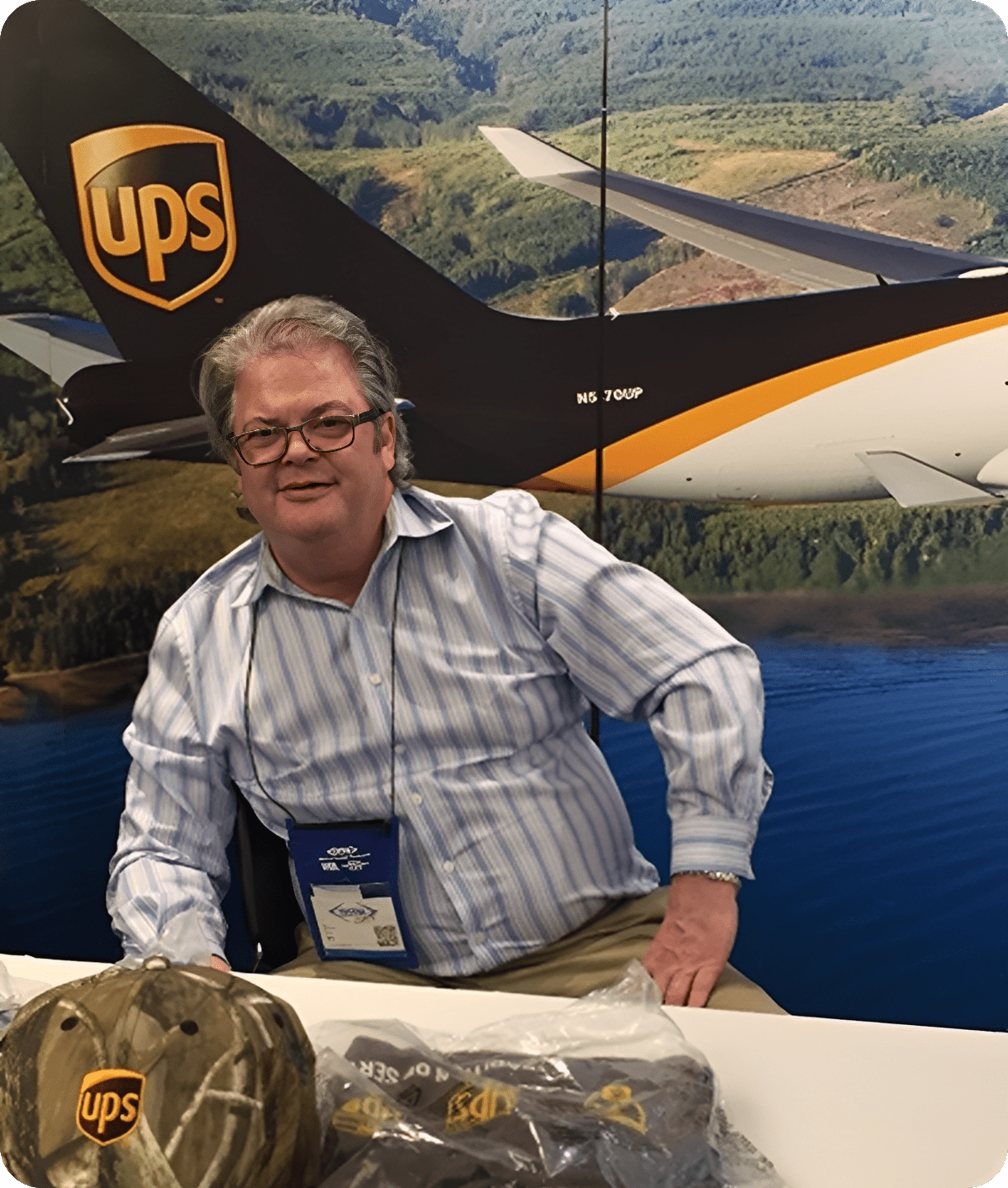 Man smiling in front of UPS airplane model at an event booth.