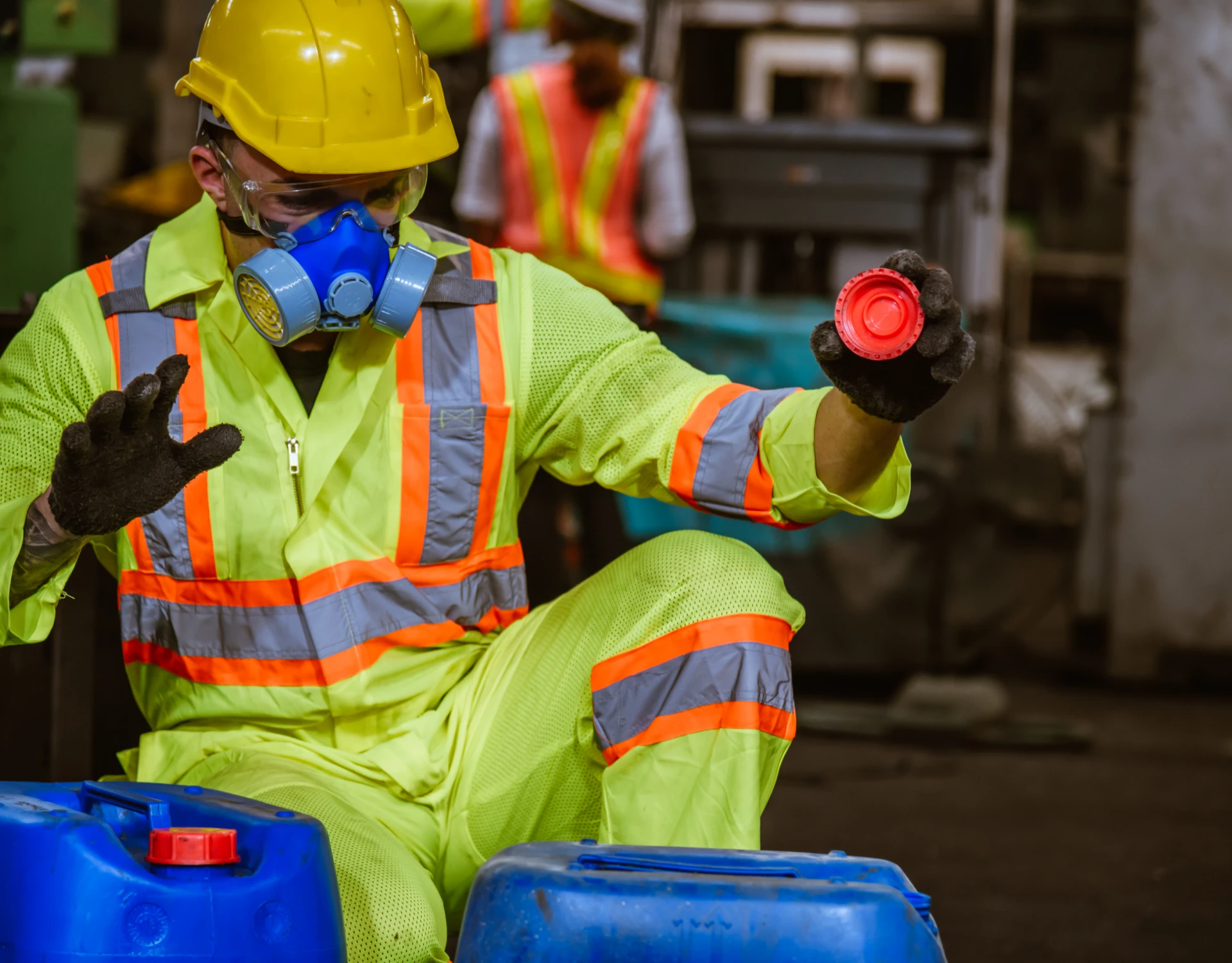 Worker handling chemical containers with safety gear.