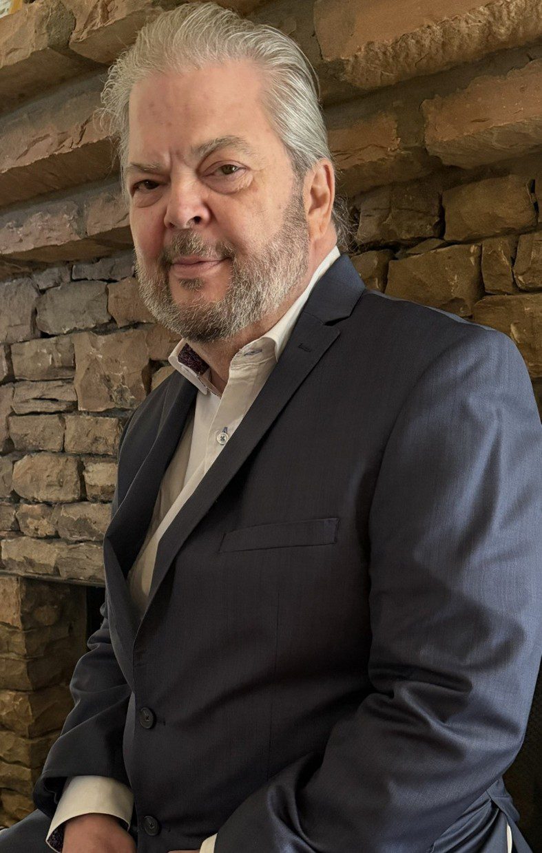 Man in a dark suit standing in front of a stone wall.